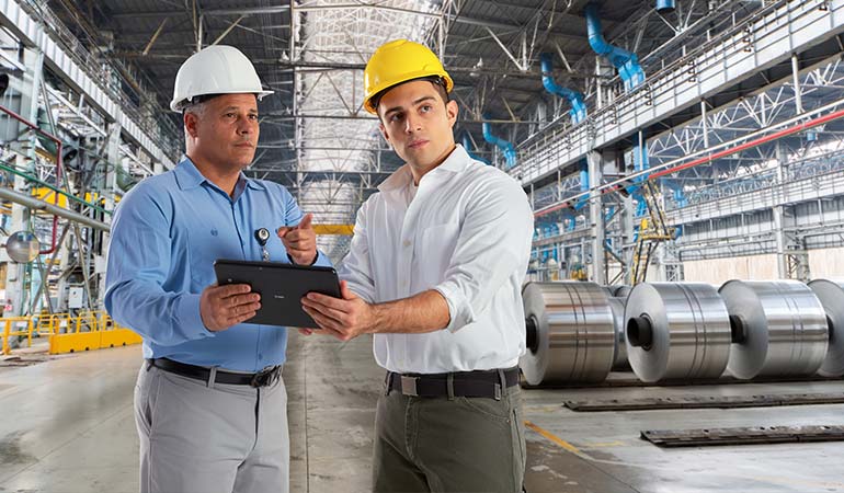 Two men in a warehouse with hardhats holding a tablet.