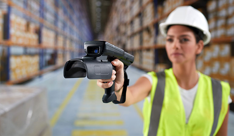 A construction worker pointing a barcode scanner in a warehouse aisle.